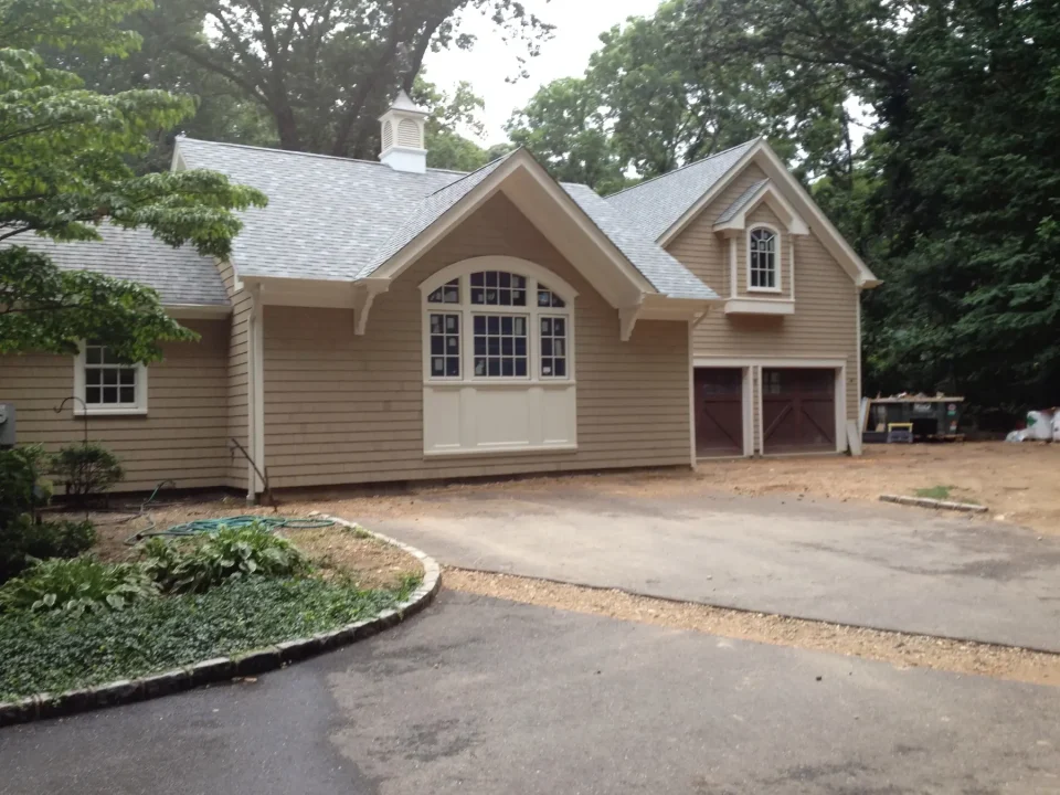 Beige house with a garage and arched windows, surrounded by trees.