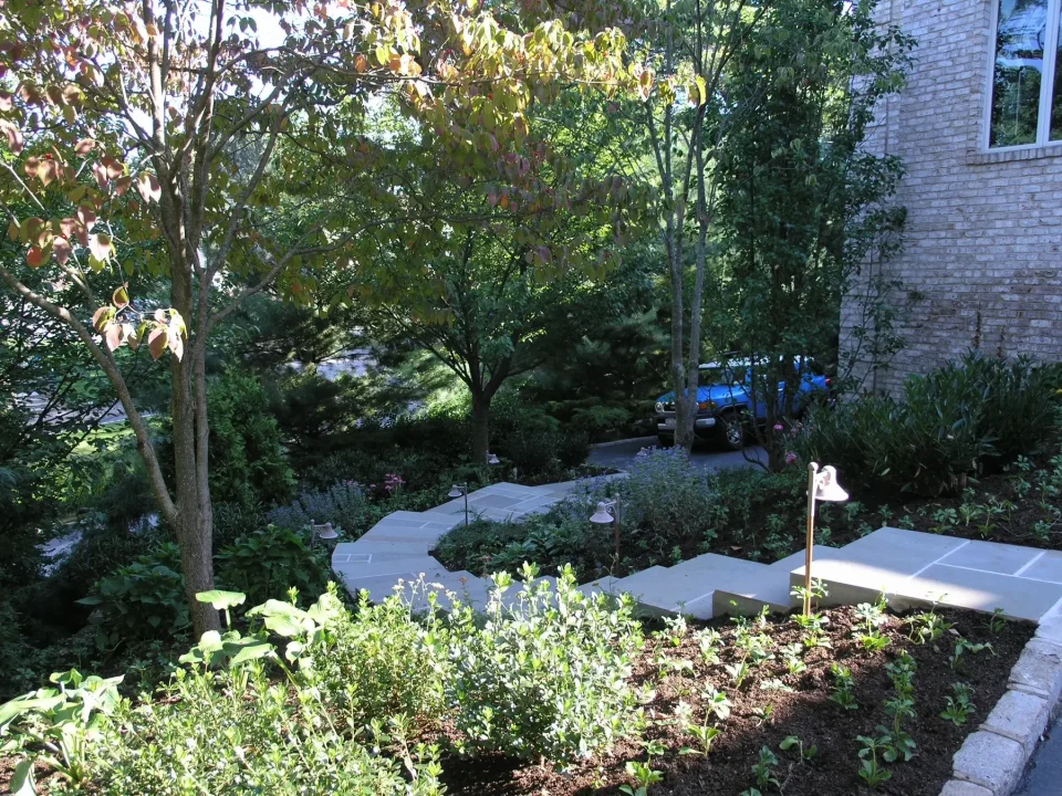 Lush garden with pathway, trees, and a partial view of a brick house.