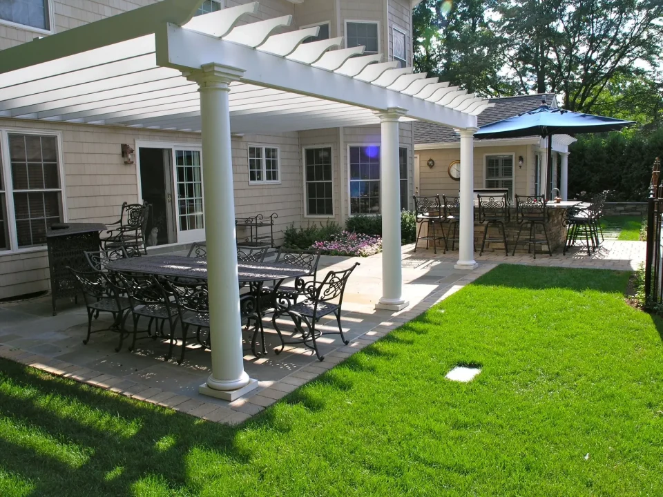 A well-manicured backyard with patio furniture, pergola, and an umbrella.