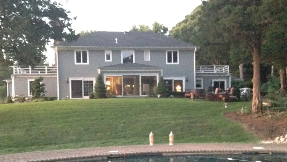 A two-story house at dusk with lit interior and a pool in the foreground.