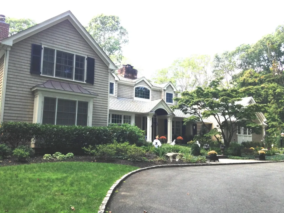 A gray two-story house with a landscaped garden and curved driveway.
