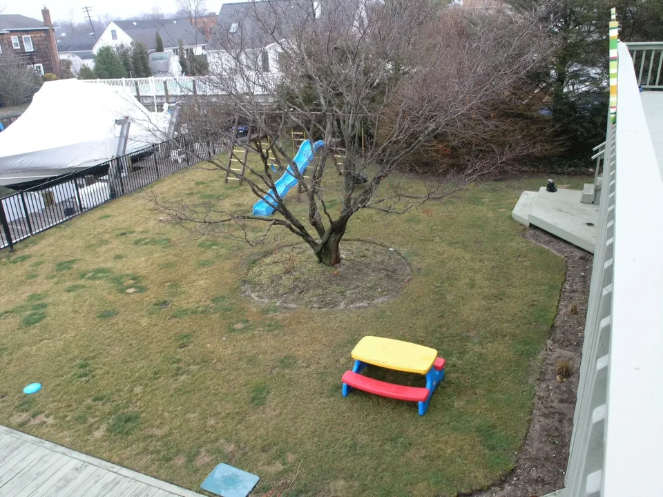 Aerial view of a backyard with a tree, lawn, kids' slide, and a colorful plastic table.