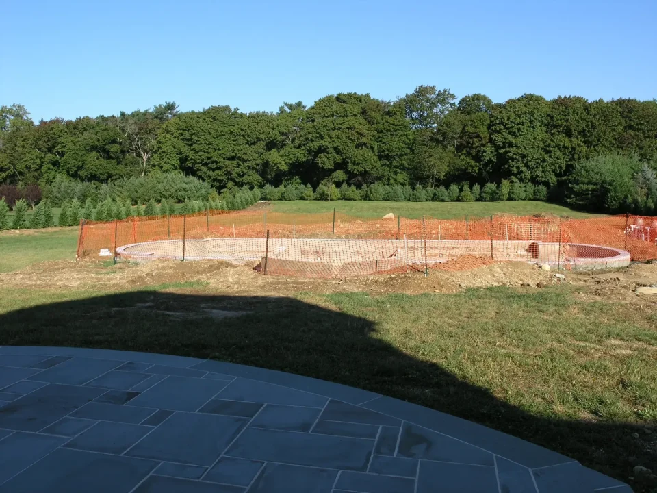 Construction site with orange fencing and early foundation stages amidst green trees.