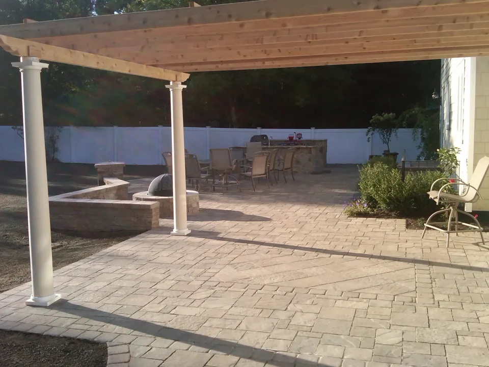 Outdoor patio with pergola, stone benches, dining table, and a bar under sunny skies.