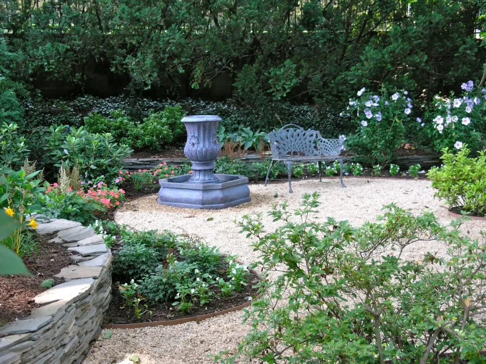 A serene garden with a stone urn, bench, and blooming plants.