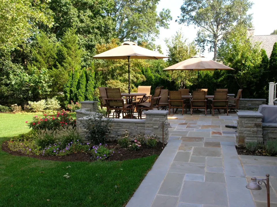 Elegant patio with furniture and umbrellas behind a lush garden