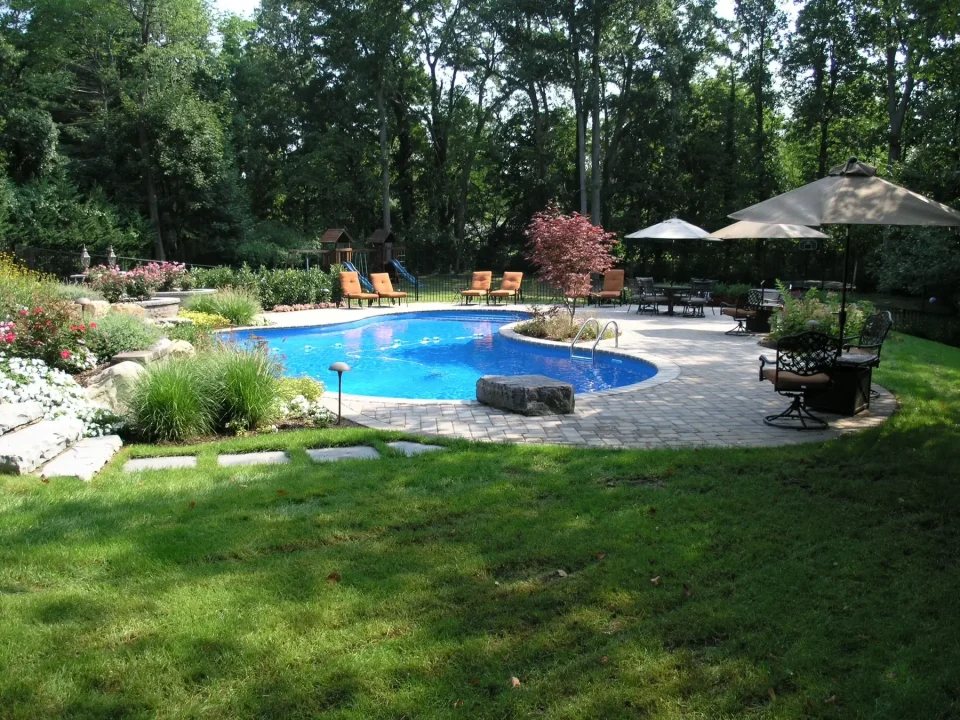 Lush backyard with a kidney-shaped pool, patio area, lounge chairs, and umbrella shades.