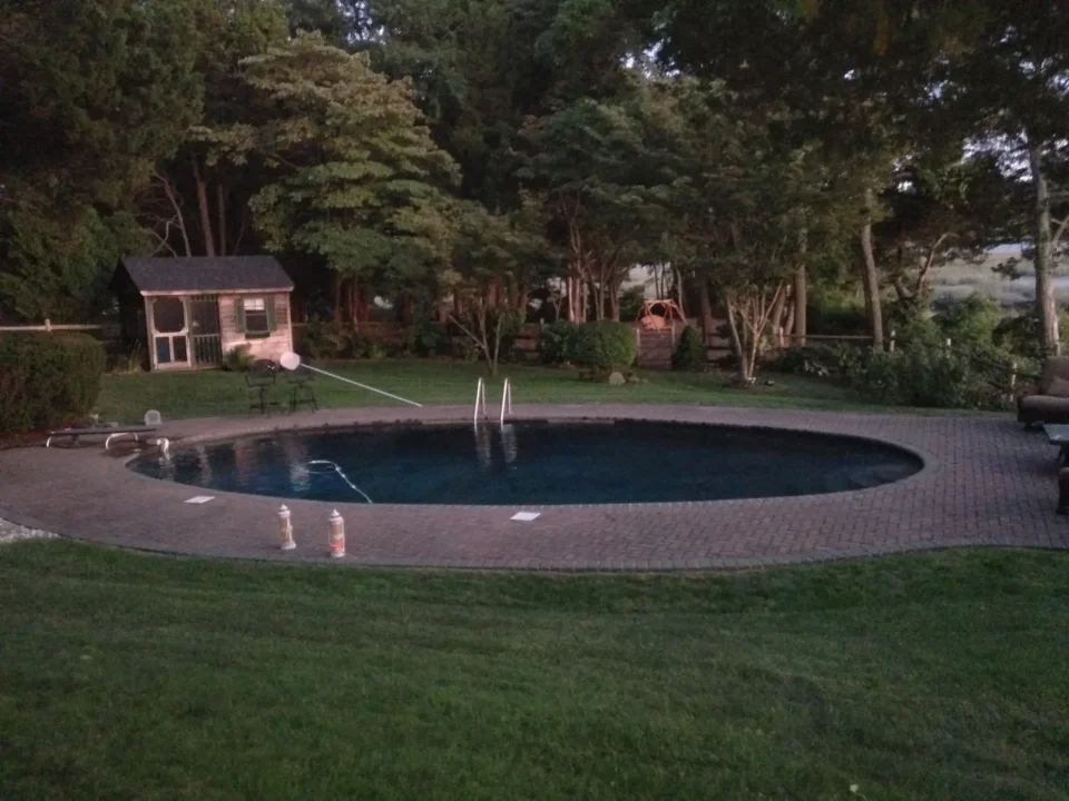 A serene backyard at dusk with an oval swimming pool, patio, and small garden shed.