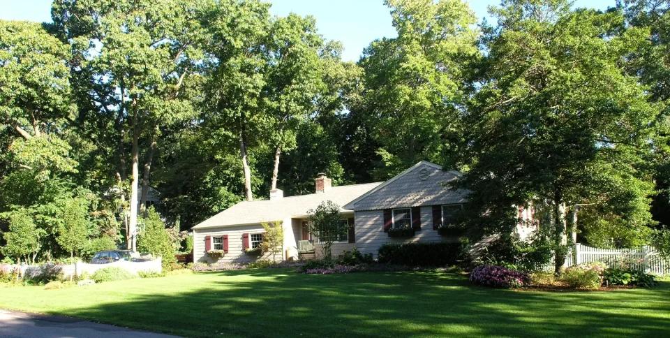 Single-story house with a gray roof, surrounded by trees and a manicured lawn.