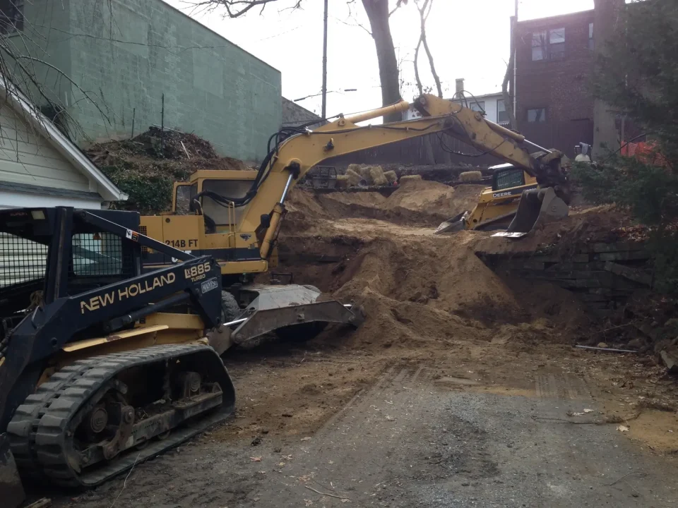Two excavators on a construction site with dug up earth and retaining walls.