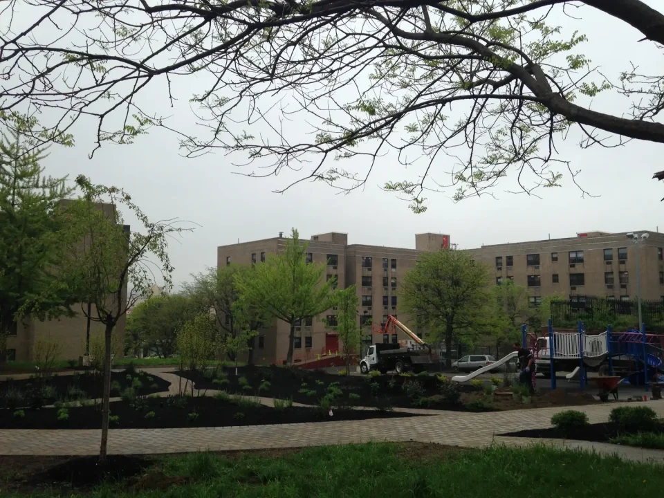 A playground and garden in an urban courtyard with buildings in the background on an overcast day.