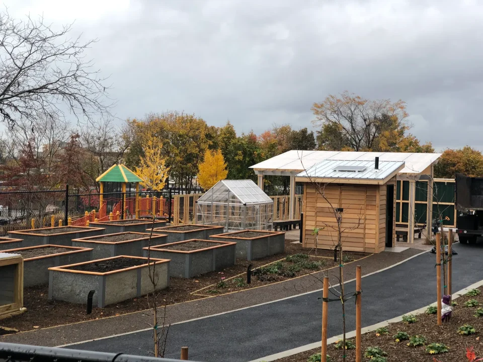 Community garden with raised beds and a greenhouse near a playground during autumn.