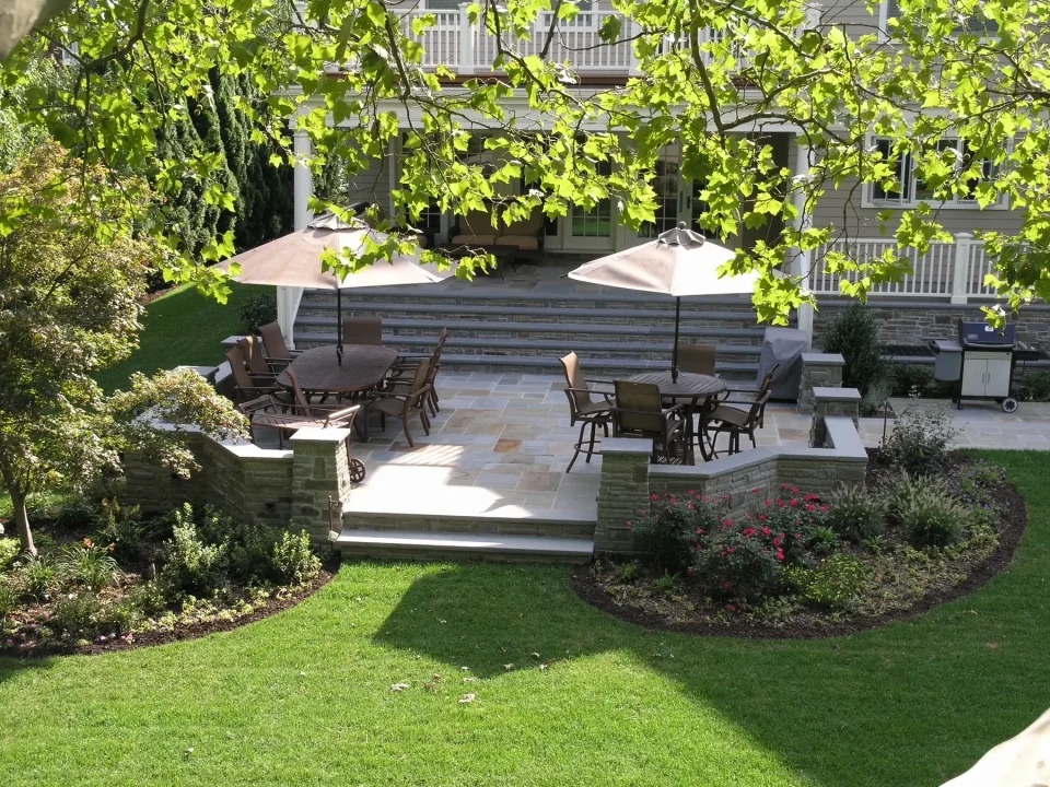 Elegant backyard patio with dining set, umbrellas, and landscaped garden, viewed from above through leaves.
