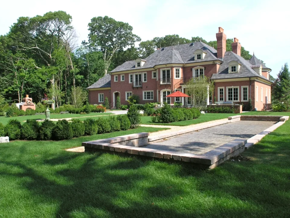 Large brick house with green lawn and garden on a sunny day.