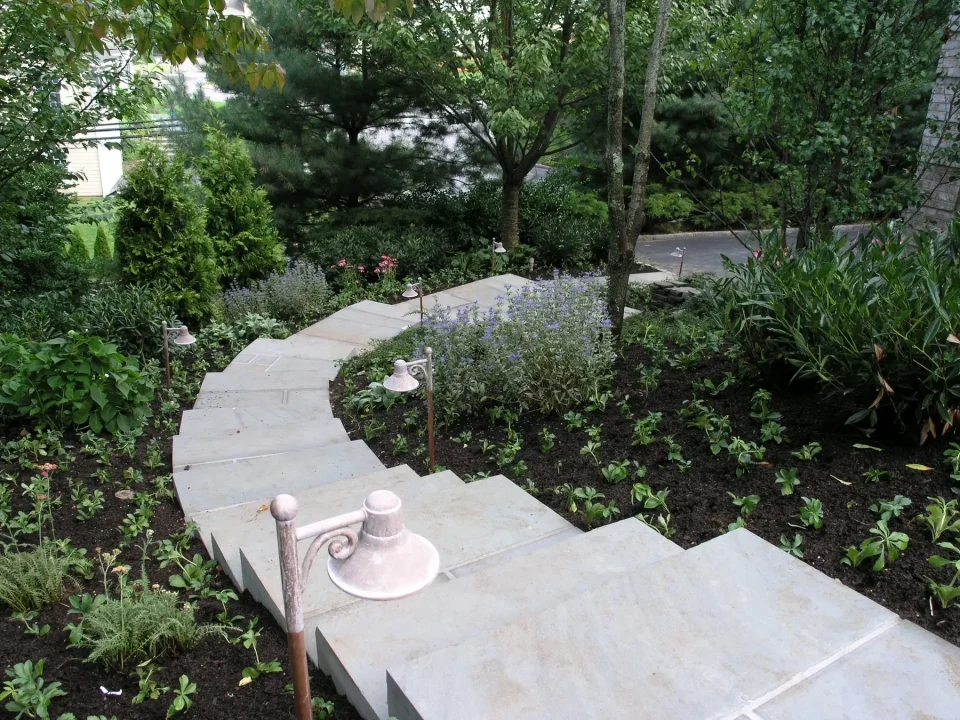 A winding stone pathway lined with green plants and small lamps in a lush garden.