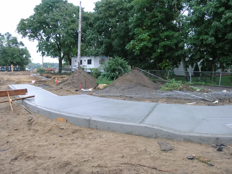 Freshly poured concrete sidewalk at a construction site with dirt and equipment.