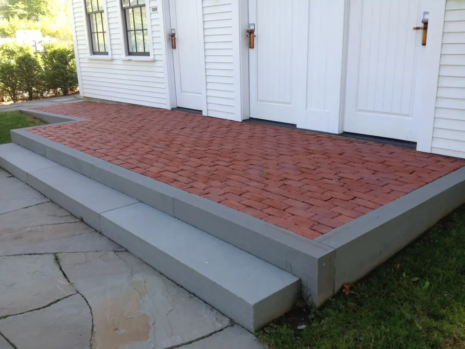 Red brick platform with concrete steps in front of white double doors.