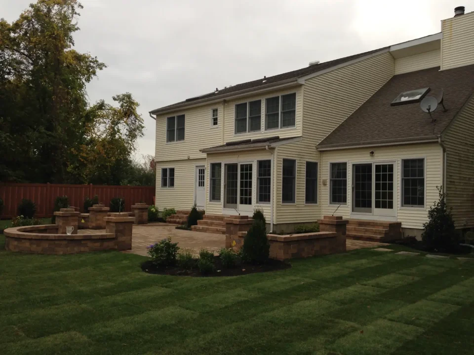 A beige two-story house with a brick patio and landscaped yard.