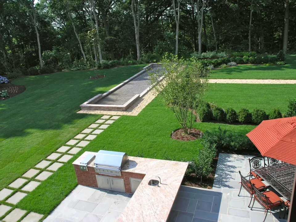 Elevated view of a backyard with a long pool, patio area, outdoor kitchen, and landscaped garden.