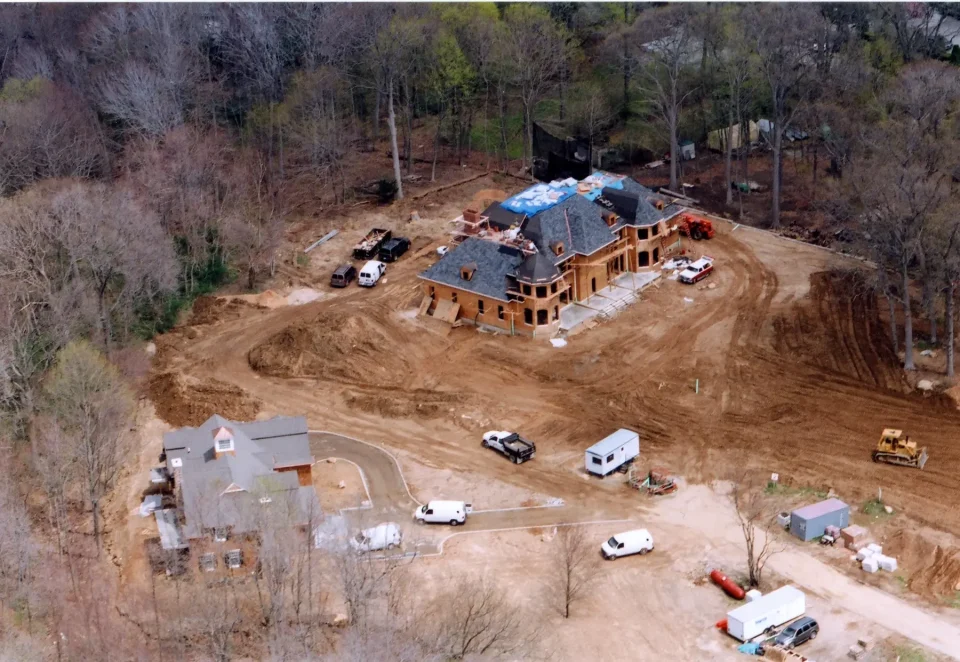 Aerial view of a large house under construction with vehicles and construction materials around.