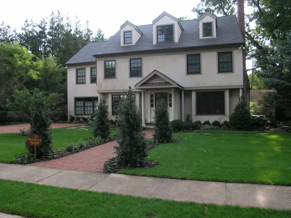 Two-story stucco house with dark roof, dormer windows, and landscaped front yard.