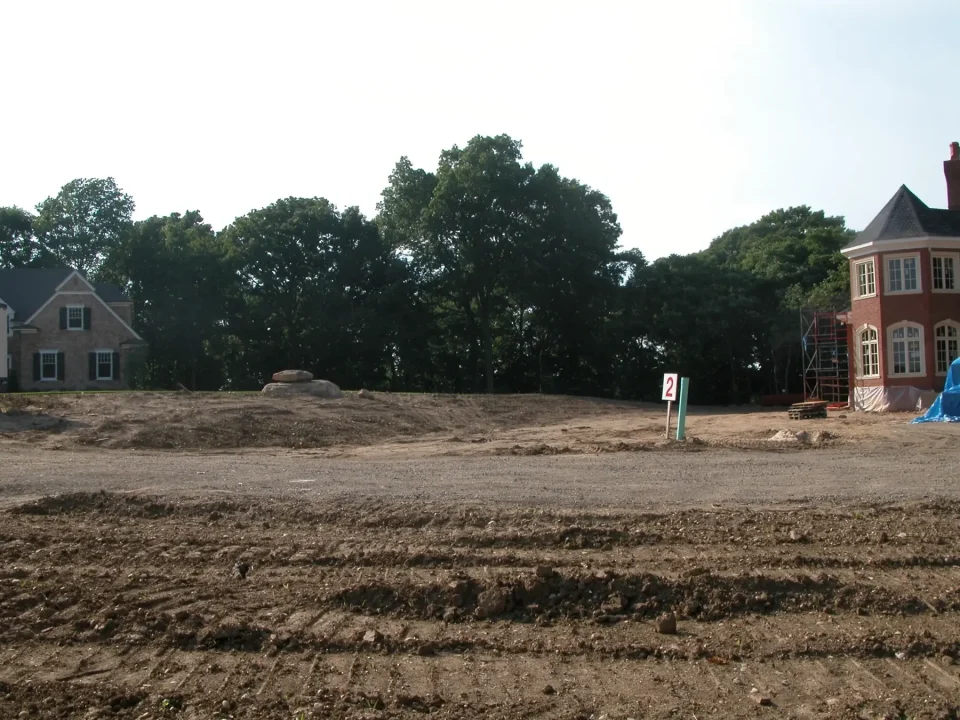 Construction site with disturbed soil and two partially built houses under a clear sky.