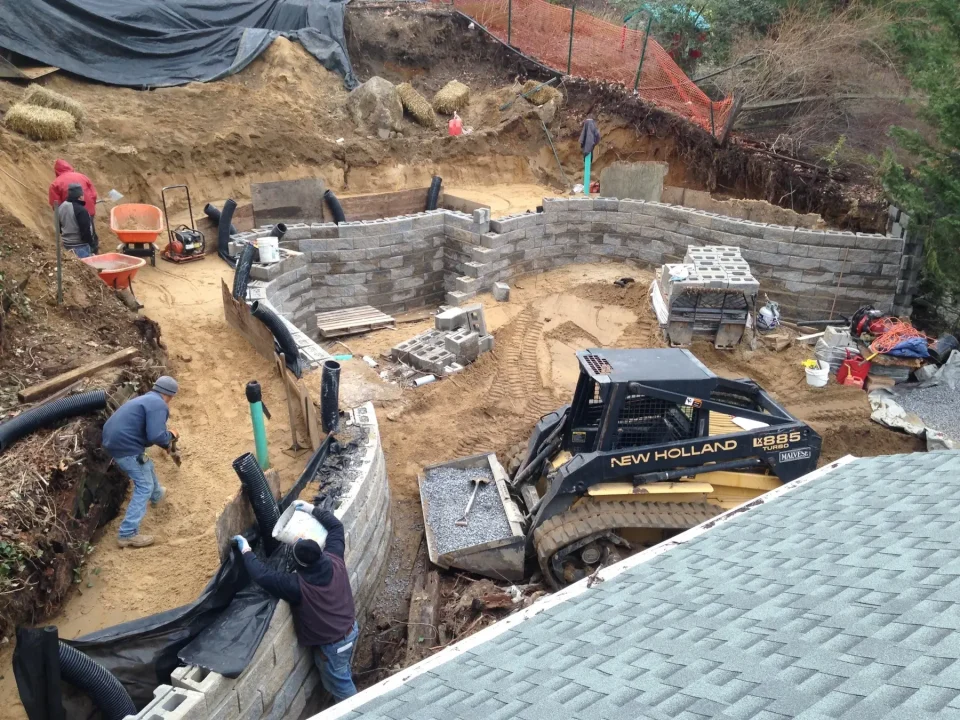 Workers and machinery at an outdoor retaining wall construction site.