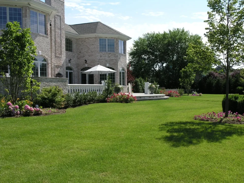 Luxurious house with manicured lawn, flowerbeds, gazebo, and a white patio.