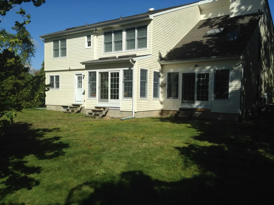 A two-story house with white siding and black shutters on a sunny day