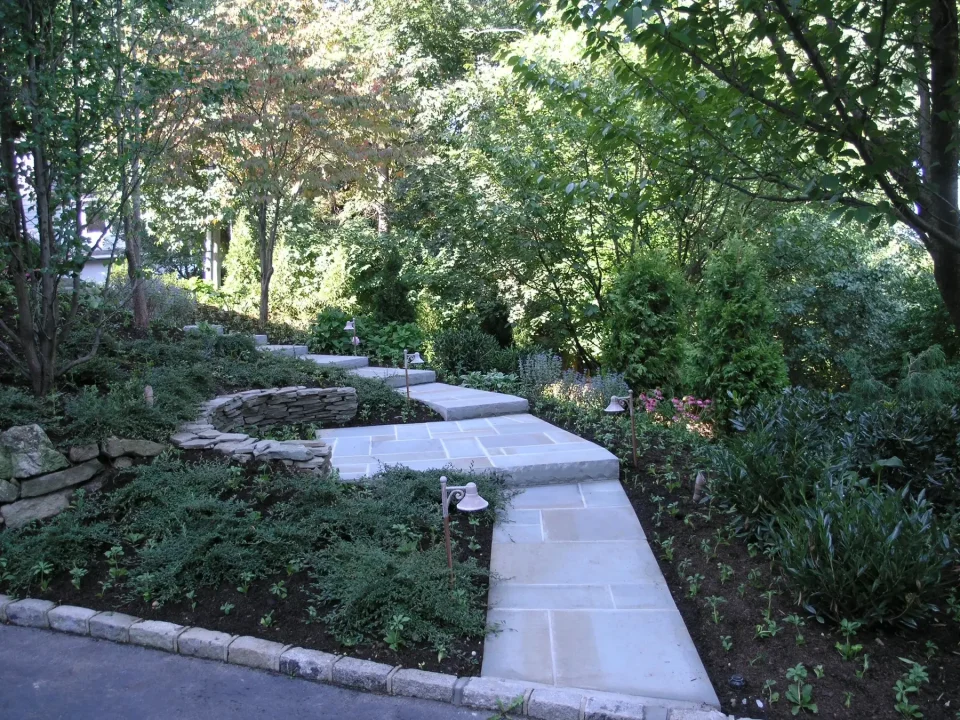 Serene garden walkway with stone steps, surrounded by lush greenery and flowers.