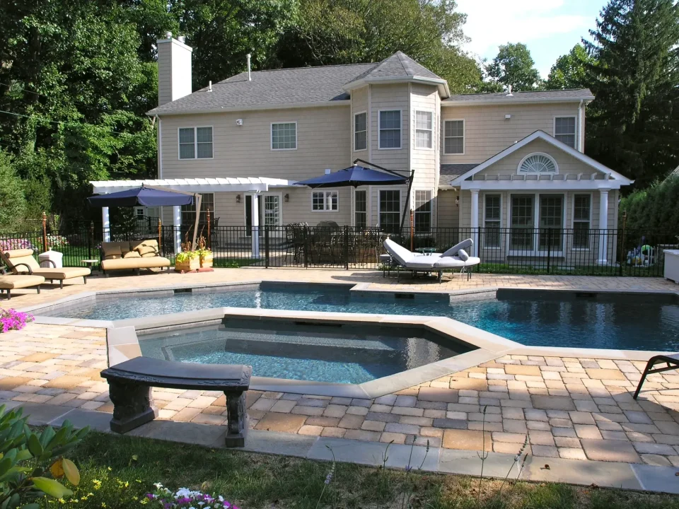 Backyard with a pool, hot tub and a two-story house with a sunshade and loungers.