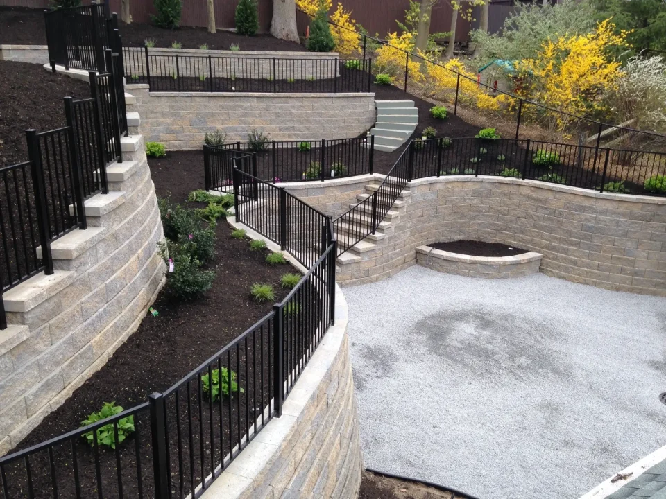 Landscaped garden with terraced stone walls and metal railings, gravel area, and staircases.