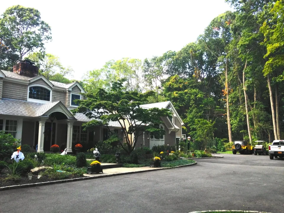 Suburban house with landscaped garden and vehicles parked by the woods.