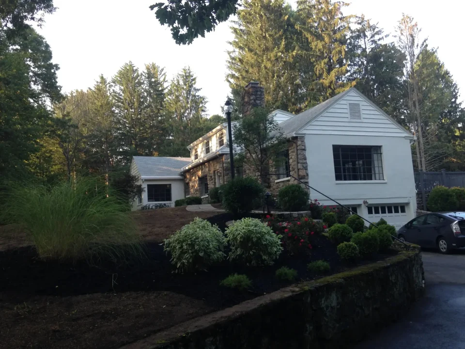 Stone and white house with landscaped garden and a car parked outside.