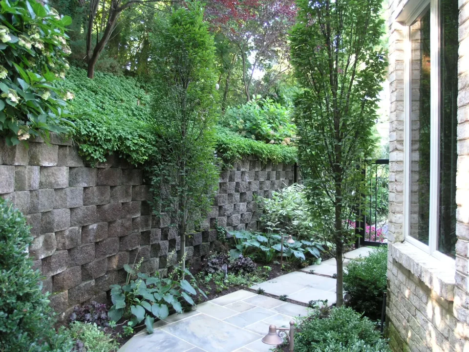 Lush garden with stone walls and pathway beside a house.
