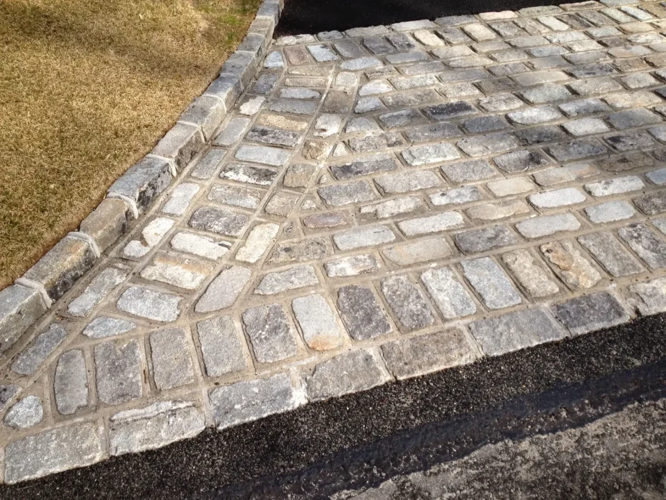 Stone paved driveway with grass edge and asphalt street transition.