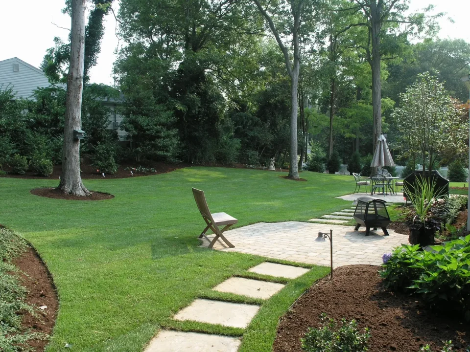 A well-manicured garden with a path, trees, bench, and outdoor seating area.
