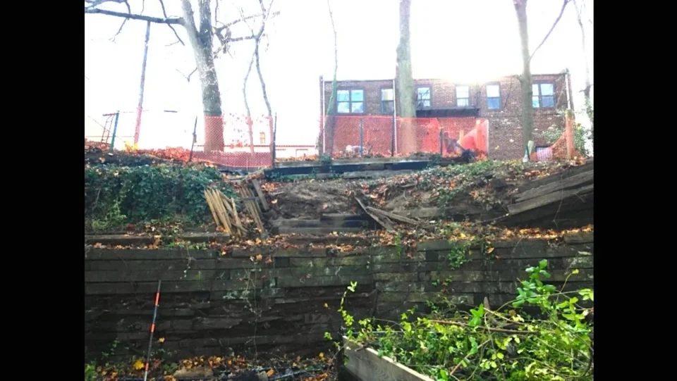 A dilapidated wooden staircase in disrepair leading up to a fenced-off construction site.