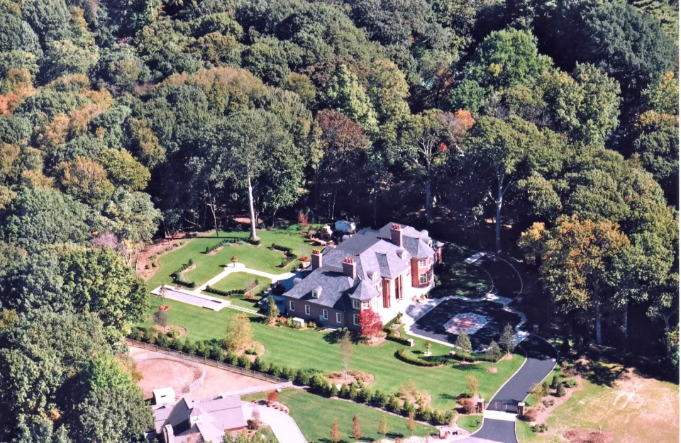 Aerial view of a large estate with a red-roofed house, surrounded by lush trees.