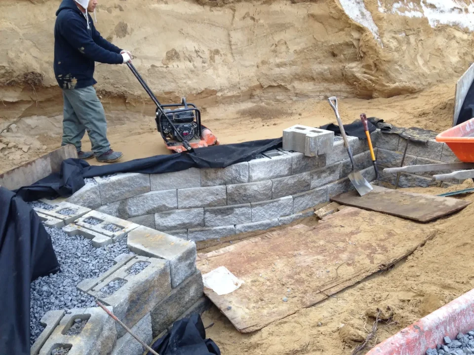 Construction of a stone retaining wall with gravel and tools around.
