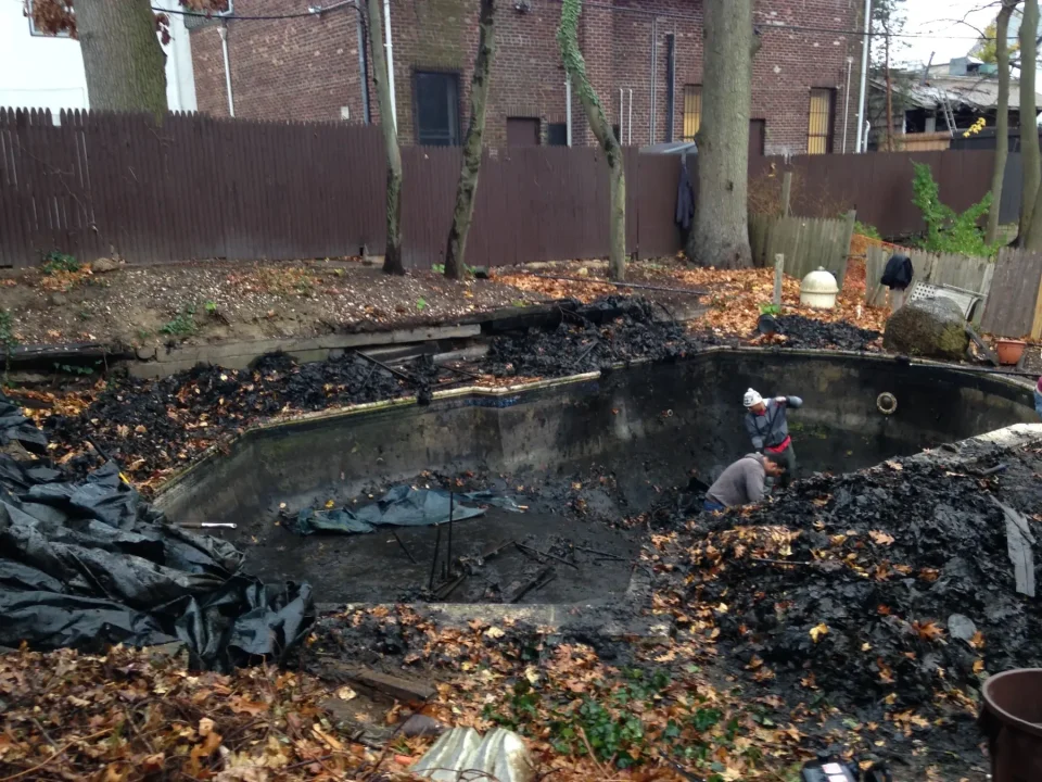 A person cleaning an empty, dirty swimming pool filled with leaves.