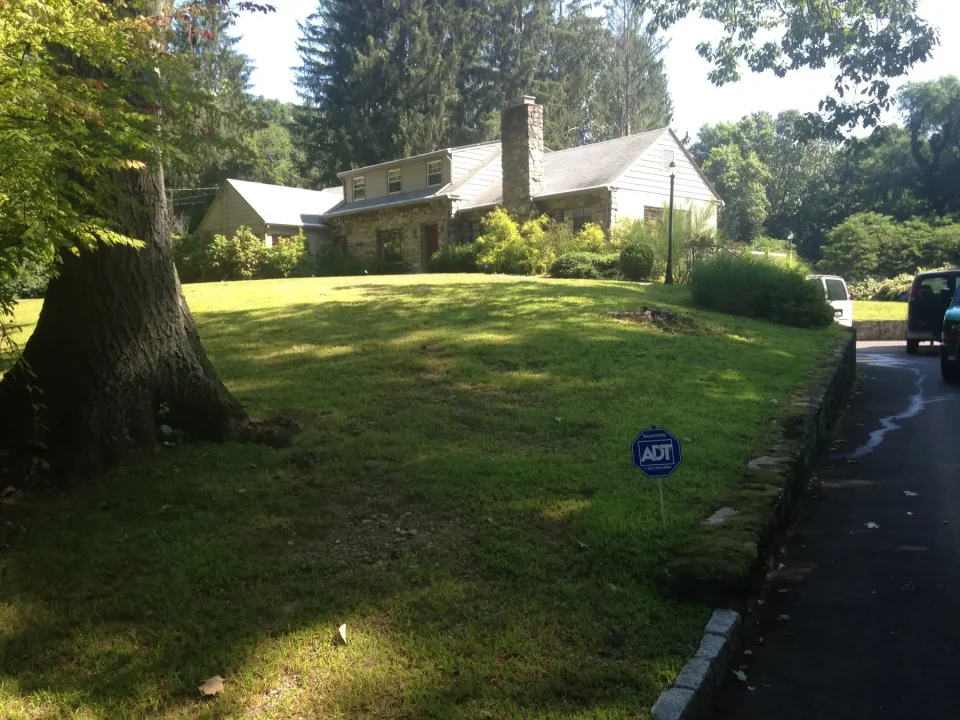 Suburban house with a large tree, a well-manicured lawn, and an ADT security sign.