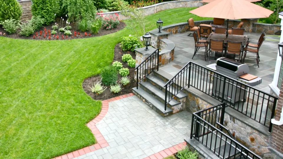 Elegant backyard with patio furniture, umbrella, manicured lawn, and stone steps.
