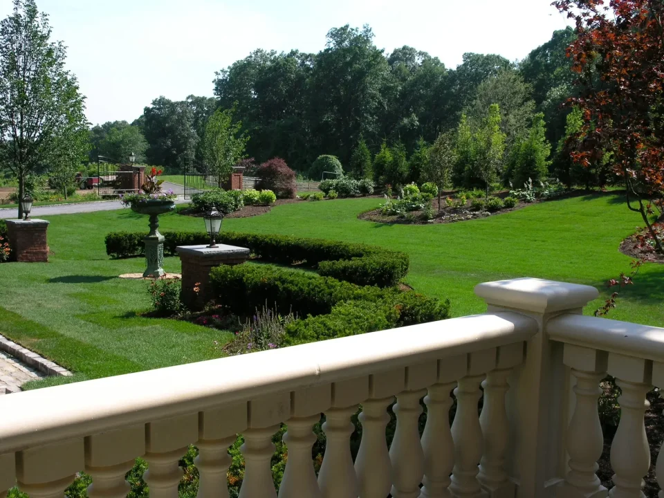 View of a landscaped garden with manicured lawns and shrubs from a balustraded balcony.