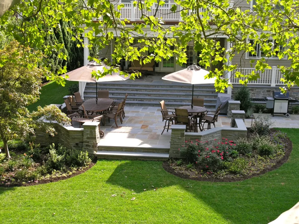 Elegant backyard patio with dining furniture, umbrellas, and surrounding gardens.