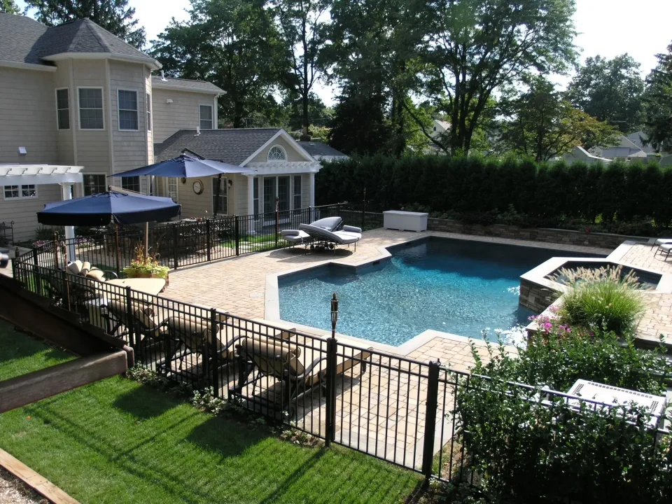 Backyard with a pool, patio, furniture, and a beige house surrounded by greenery.