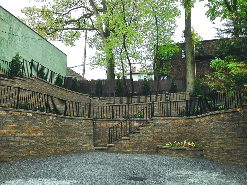 Stone steps leading to a gated garden with trees and a building in the background.