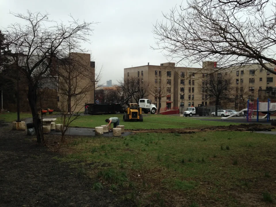 Wet urban park with bare trees, playground, construction equipment, and vehicles.
