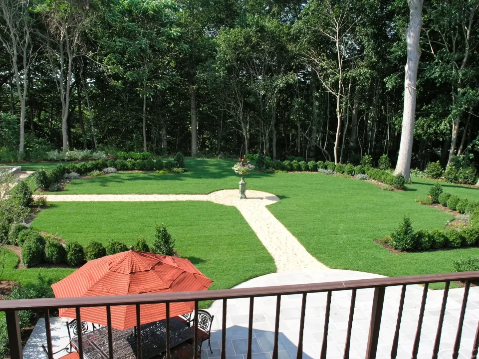 Well-manicured garden with pathways, lawn, and an umbrella on a patio, viewed from above.
