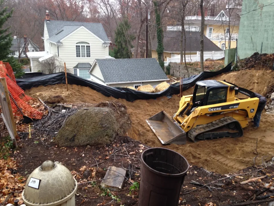 Construction site with a skid steer loader, large boulders, and erosion control barriers.